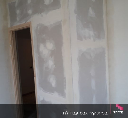 קיר גבס עם חיבורים מטויחים ליד דלת עץ